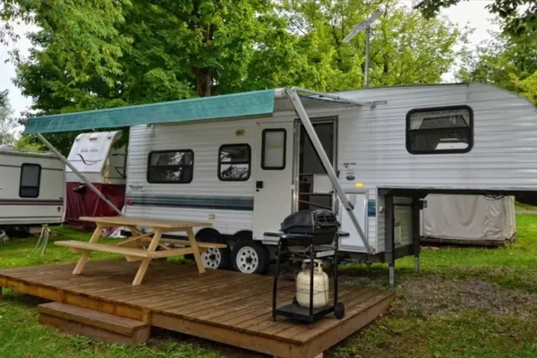 Caravane stationnée avec terrasse en bois et barbecue.