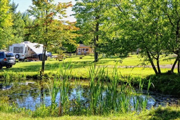 Camping avec caravanes près d'un étang entouré d'arbres.