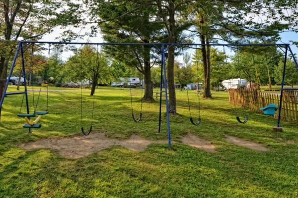 Aire de jeux avec balançoires dans parc verdoyant.