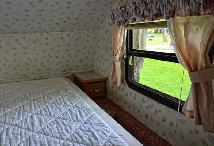 Intérieur spacieux d'une roulotte, lit et fenêtre.